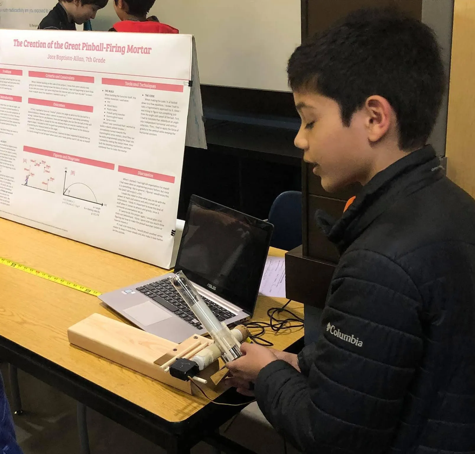 Jace in seventh grade holding the pinball cannon in front of his science-fair poster
